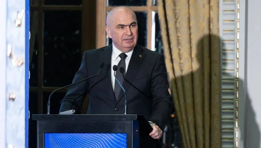 Un bărbat cu părul scurt și costum negru stă în spatele unui podium cu microfoane.