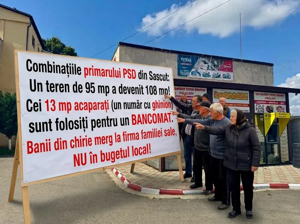 Un grup de persoane stă lângă un panou informativ mare pe care este scris un text cu litere negre și roșii sub un cer senin.