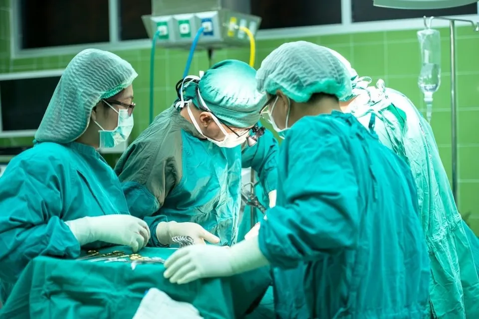 Patru medici în halate și căciuli verzi de operație stau în jurul unei mese de intervenție într-o sală de spital.