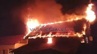 Un acoperiș de casă este acoperit de flăcări intense pe un fundal întunecat de noapte.