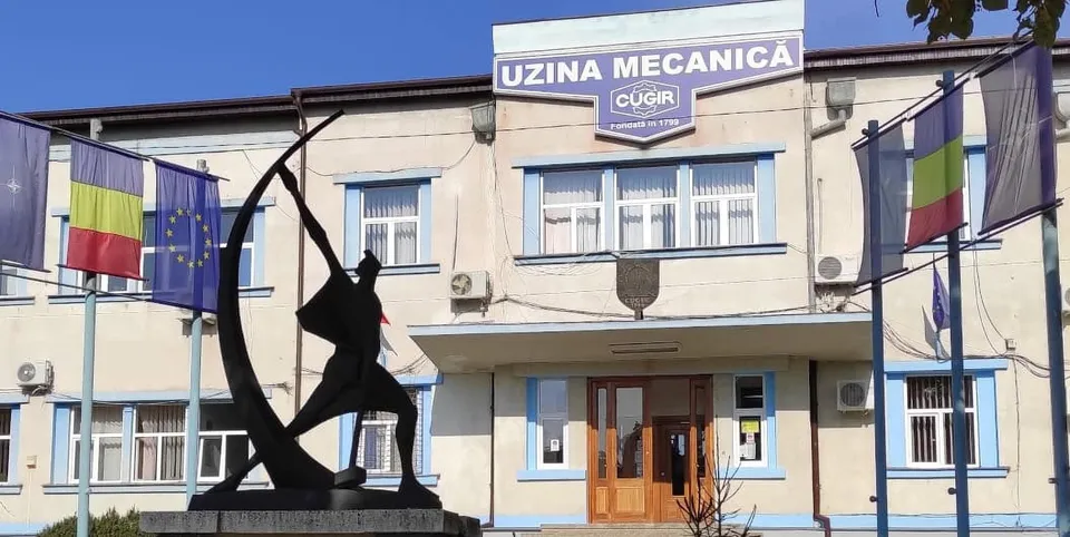 O statuie neagră reprezintă o siluetă umană în mișcare lângă o clădire cu ferestre și diverse steaguri afișate pe fațadă.