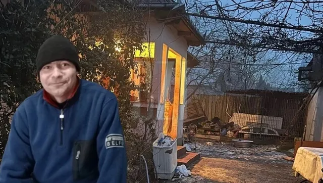 Un bărbat cu căciulă neagră și hanorac albastru stă în fața unei case cu lumină aprinsă în interior și un curte cu vegetație uscată.