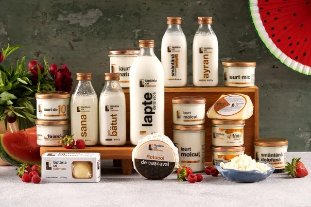 Diverse produse lactate, precum lapte, iaurt și brânză, sunt așezate pe o suprafață lângă fructe și flori.