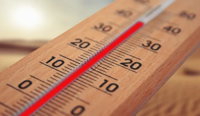 Un termometru de lemn cu o coloană de lichid roșu indică o temperatură ridicată sub un cer luminos.