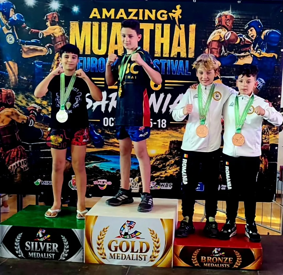 Patru copii stau pe podiumuri marcate cu medalii de aur, argint și bronz, purtând medalii și echipamente sportive în fața unui panou colorat.