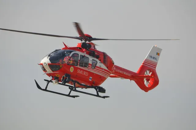 Un elicopter roșu și alb cu inscripția SMURD zboară pe un cer gri.