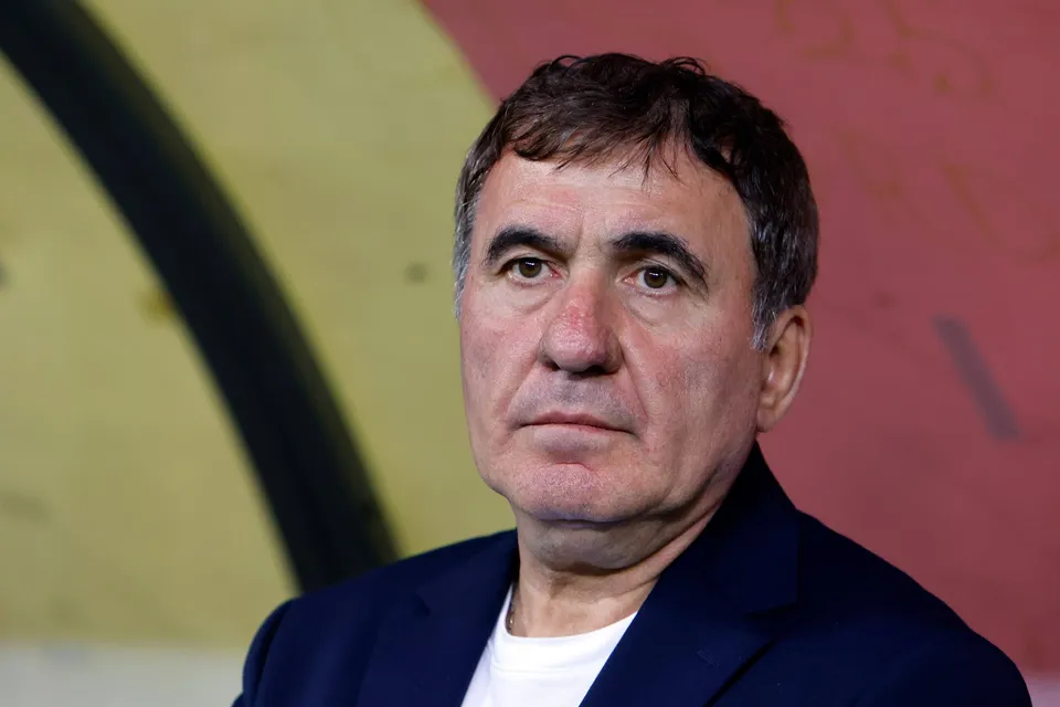Un bărbat cu părul scurt și închis la culoare poartă un sacou albastru peste un tricou alb, privind spre lateral.