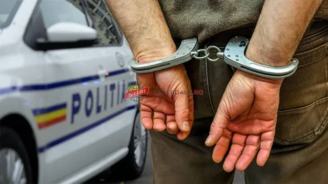 Mâinile unui bărbat sunt prinse în cătușe metalice, fiind poziționate în spatele corpului, cu un autovehicul de poliție alb în fundal.