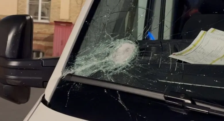 O parțișcă de sticlă de la parbrizul unui vehicul alb este spartă și crăpată într-un punct central.