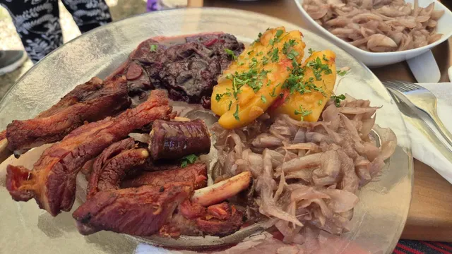 O farfurie mare cu carne de porc friptă, costuri, zăcări de cartofi galbeni ornate cu pătrățele verzi, vară roșie și ceapă roșie tocată fin.