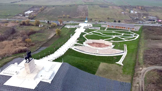 O vedere aeriană prezintă un monument cu o statuie călare, un drum alb, un amfiteatru și zone verzi într-un peisaj rural.
