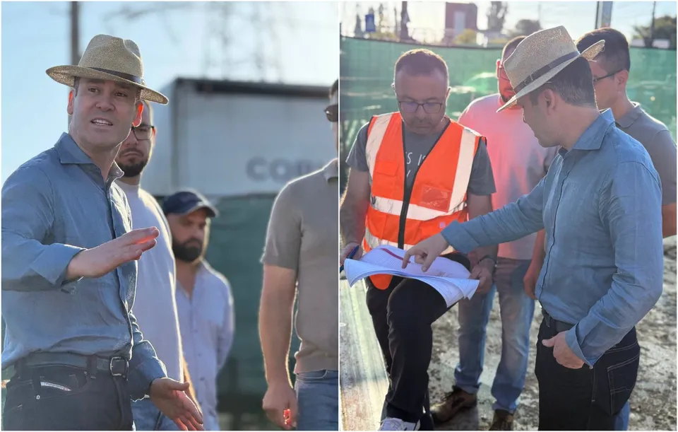 Un bărbat cu pălărie și cămașă albastră arată ceva către un grup de oameni lângă un șantier.