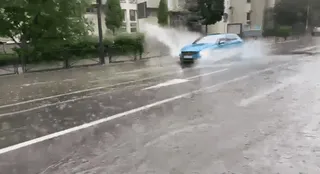 Un autovehicul albastru circulă pe un drum umed, ridicând o spray de apă din cauza unei bălți.