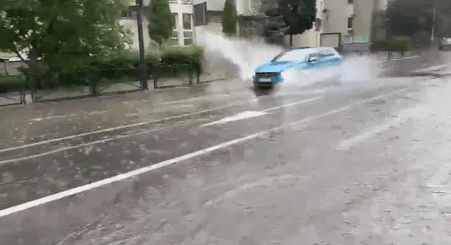 Un autovehicul albastru circulă pe un drum umed, ridicând o spray de apă din cauza unei bălți.