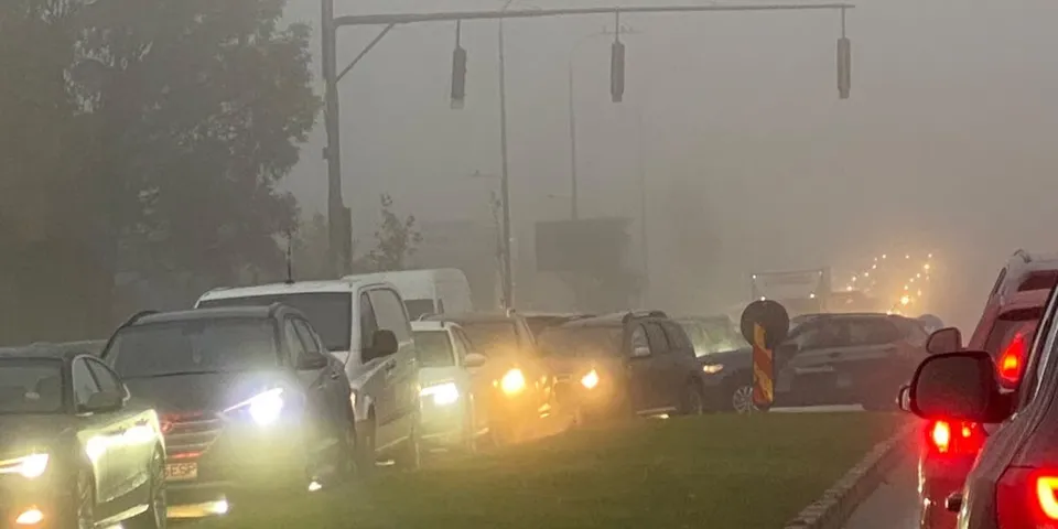 Mai multe mașini cu farurile aprinse circulă pe un drum într-o vizibilitate redusă din cauza unei ceață dense.