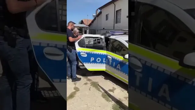 Un bărbat este escortat de un polițist către o mașină de poliție, cu ușa deschisă, în fața unei case.