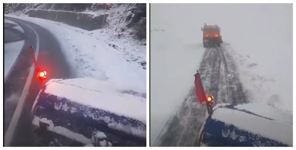 Vehiculul acoperit cu zăpadă are luminile roșii aprinse pe un drum înzăpezit, în timp ce un autovehicul galben deszăpezește drumul în față.