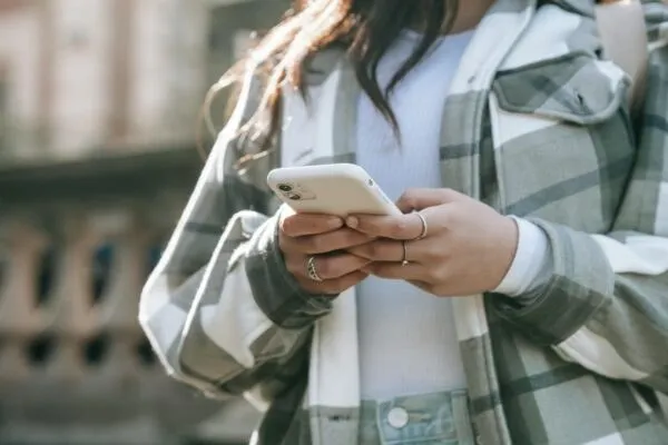 O persoană poartă o jachetă în culori gri și alb și ține un telefon mobil cu ambele mâini.