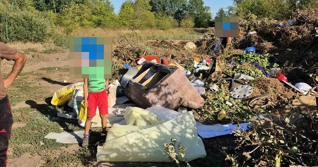 O persoană în bermudaج roșii și tricou verde stă lângă un morman de deșeuri compus din obiecte diverse, materiale de construcții și resturi vegetale.