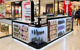 Un stand de prezentare de tip kiosk într-un centru comercial expune diverse accesorii pentru telefoane mobile pe rafturi iluminate.