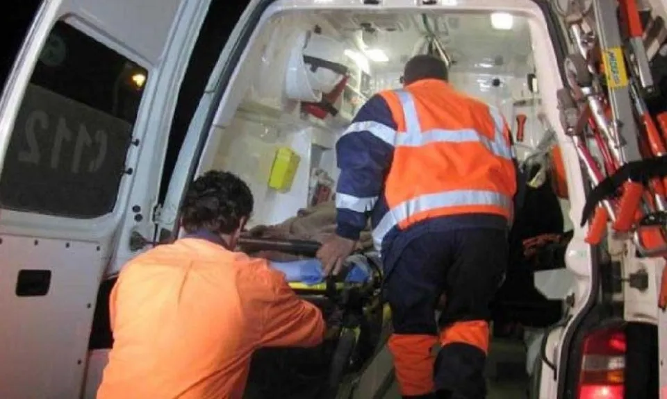 Două persoane purtând veste reflectorizante lucrează în interiorul unei ambulanțe deschise noaptea.