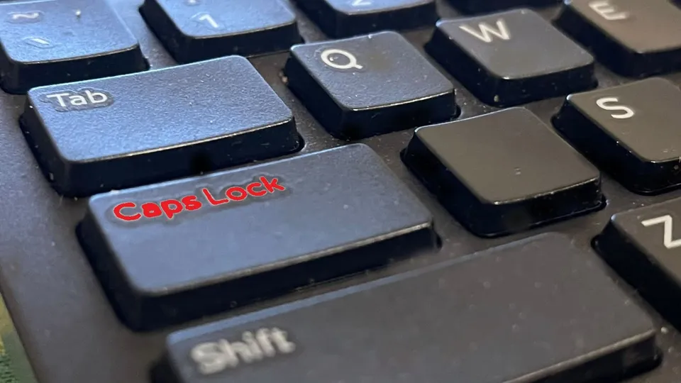 Aproape a unei taste Caps Lock pe o tastatură neagră, cu literele inscripționate în roșu, alăturate de tastele Tab, Shift și alte taste alfanumerice.
