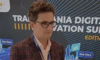 Un bărbat cu ochelari și sacou în croit este poziționat în fața unui panou grafic cu text și ilustrații digitale.