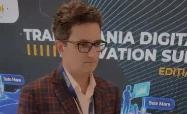 Un bărbat cu ochelari și sacou în croit este poziționat în fața unui panou grafic cu text și ilustrații digitale.