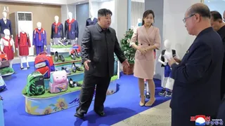 Un bărbat într-un costum închis se plimbă printr-o încăpere cu manechine îmbrăcate în haine și diverse accesorii expuse pe rafturi.