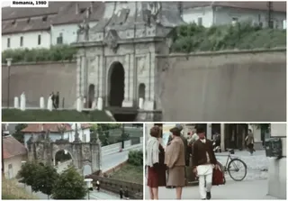 O poartă de piatră cu un arc central se află lângă un zid, în timp ce persoane merg pe un trotuar lângă o bicicletă.