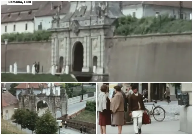 O poartă de piatră cu un arc central se află lângă un zid, în timp ce persoane merg pe un trotuar lângă o bicicletă.