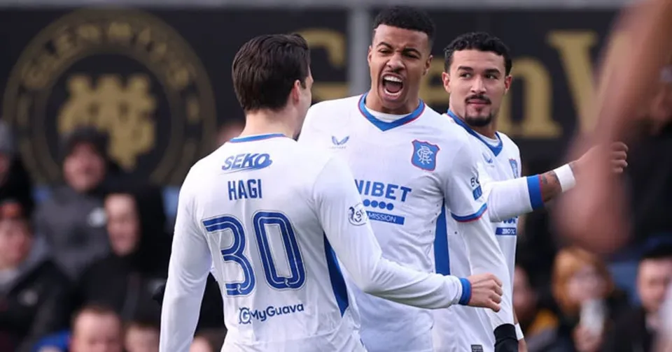 Trei jucători de fotbal în echipamente albe cu detalii albastre sărbătoresc pe un teren de sport.
