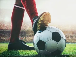 O persoană cu șosete roșii și ghete de fotbal stă pe un teren de iarbă lângă un fotbal alb și negru.
