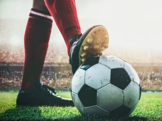O persoană cu șosete roșii și ghete de fotbal stă pe un teren de iarbă lângă un fotbal alb și negru.