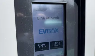 Un ecran digital afișează textul „Bine ati venit” și logoul „EVBOX” pe un dispozitiv de încărcare de culoare închisă.