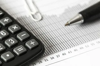 Un calculator negru, un pix și un clips metalic sunt plasate pe un document cu grafice și cifre.