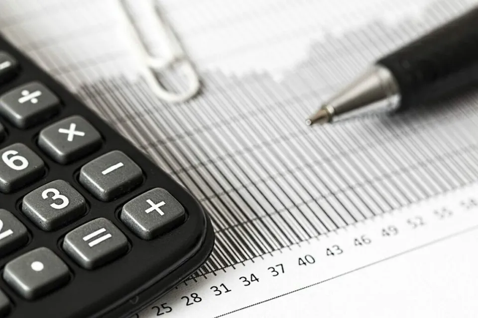 Un calculator negru, un pix și un clips metalic sunt plasate pe un document cu grafice și cifre.
