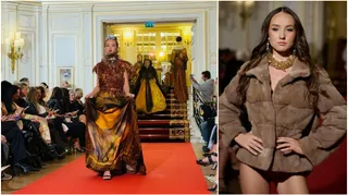 O femeie poartă o jachetă de blană maro și un colier auriu, în timp ce o altă femeie pășește pe un podium cu o rochie lungă, aurie.