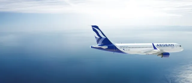 Un avion alb cu marcaje albastre zboară deasupra unei suprafețe de apă sub un cer înnorat.