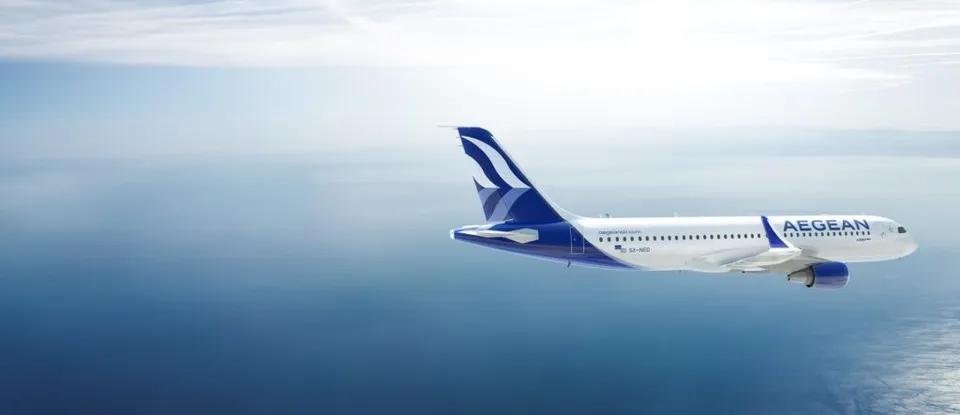Un avion alb cu marcaje albastre zboară deasupra unei suprafețe de apă sub un cer înnorat.