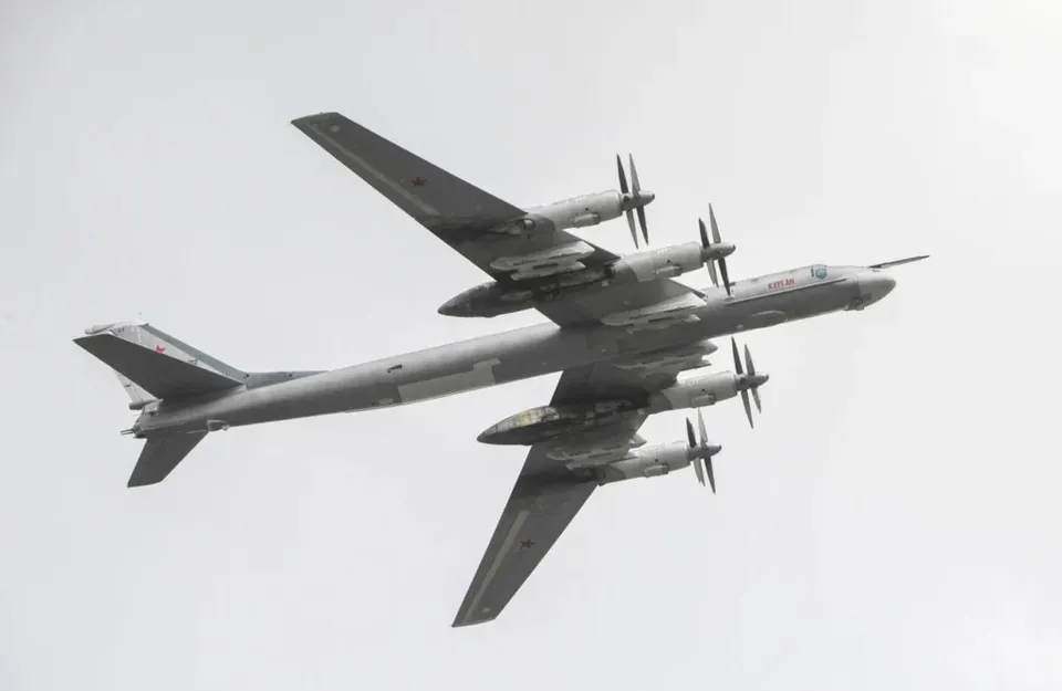 Un avion gri cu patru motoare cu elice zboară pe un cer deschis și gri.