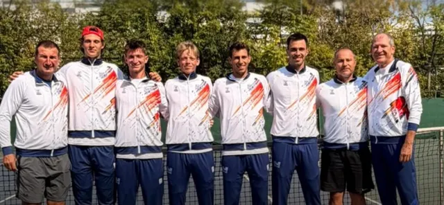 Opt bărbați în echipamente sportive albe și albastre stau în linie pe un teren de tenis în fața unor copaci verzi.