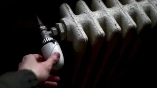 O mână reglează robinetul unui calorifer metalic alb într-un mediu întunecat.