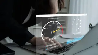O persoană în costum elegant folosește un laptop, pe fundalul căruia se proiectează o interfață digitală cu un viteza-metru și statistici de performanță a internetului.