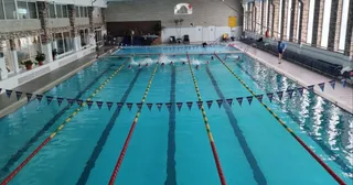 O piscină interioară cu linii de culoare albastră și marcaje de culoare galbenă și roșie, cu câteva persoane în apă la capătul bazinului.