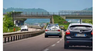 Mai multe mașini circulă pe o autostradă lângă un gard de protecție și sub un pod de beton.