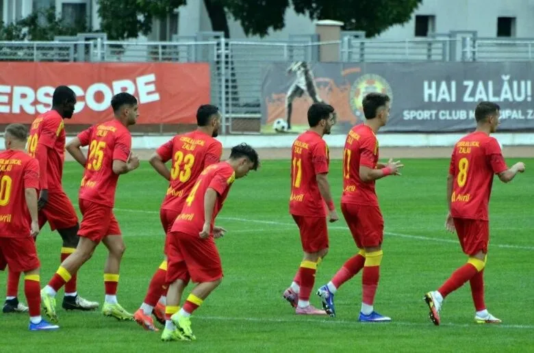 Cei opt jucători de fotbal poartă echipamente roșii și se află pe un teren de fotbal cu iarbă verde.