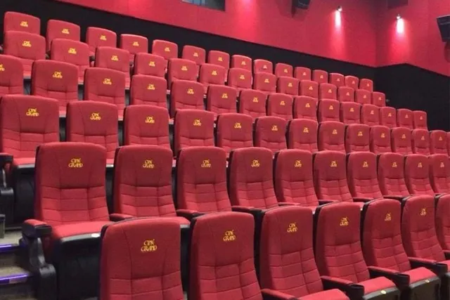 Rânduri de scaune de cinema roșii cu spătare înalte sunt așezate în interiorul unei săli întunecate.