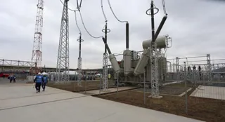 Echipamente electrice mari și turnuri metalice sunt instalate pe un teren deschis sub un cer înnorat, lângă o suprafață pavată.