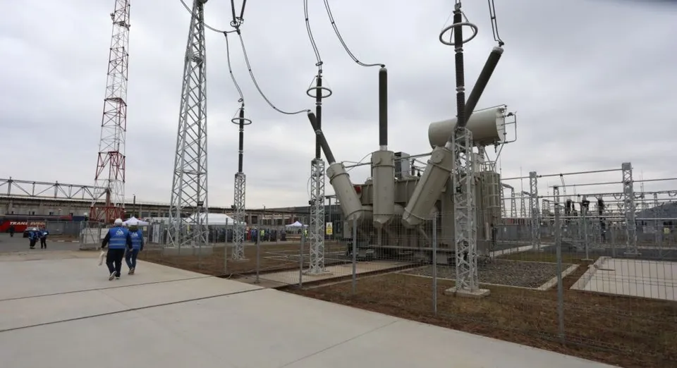 Echipamente electrice mari și turnuri metalice sunt instalate pe un teren deschis sub un cer înnorat, lângă o suprafață pavată.